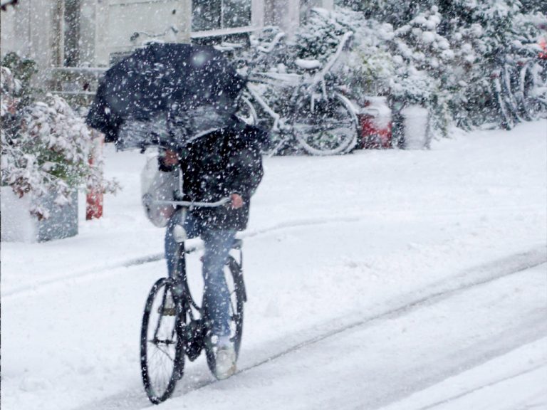 Rowerzysta pod parasolem jadący zimą